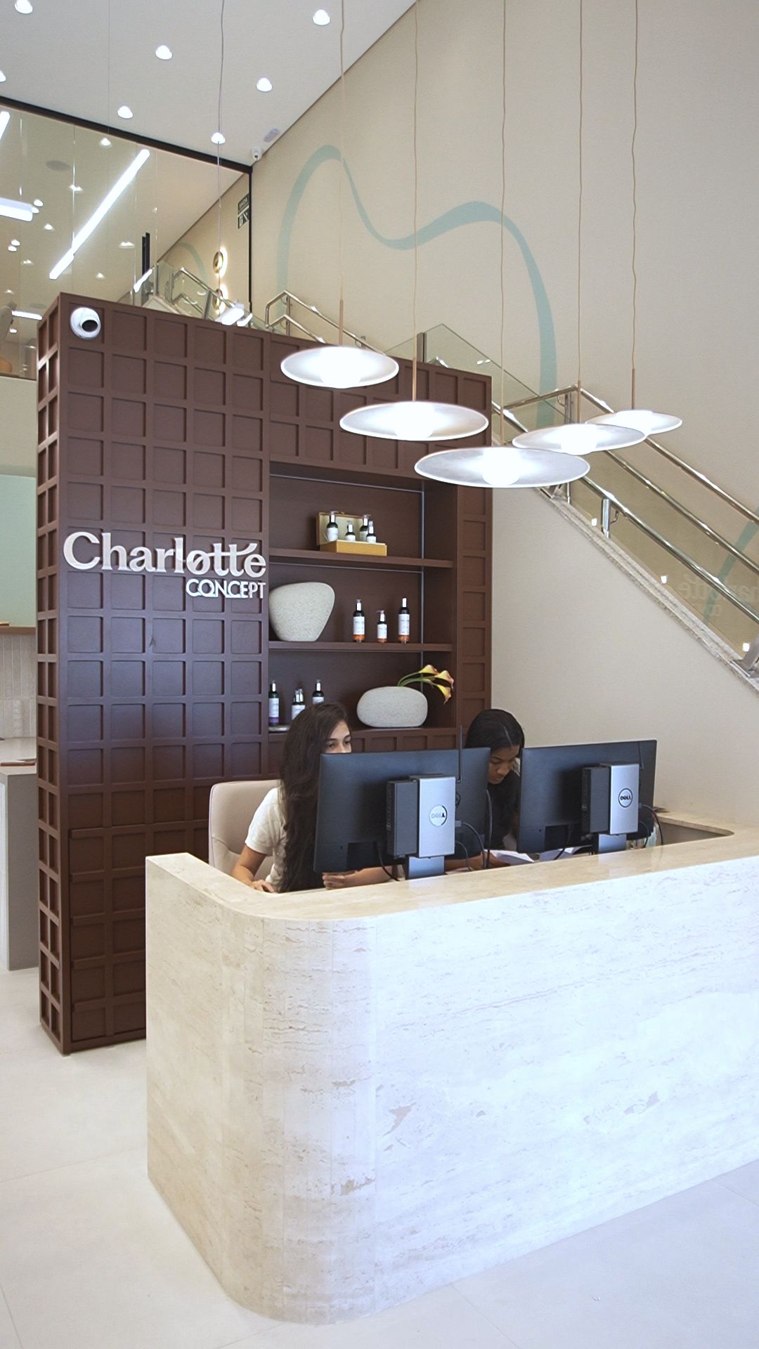 Recepção da Charlotte Concept, com o balcão, a parede da marca e a escada